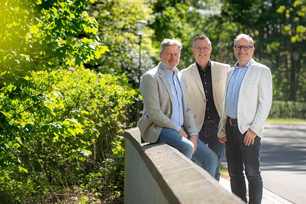 Drie makelaars buiten aan een brug voor een groene heg