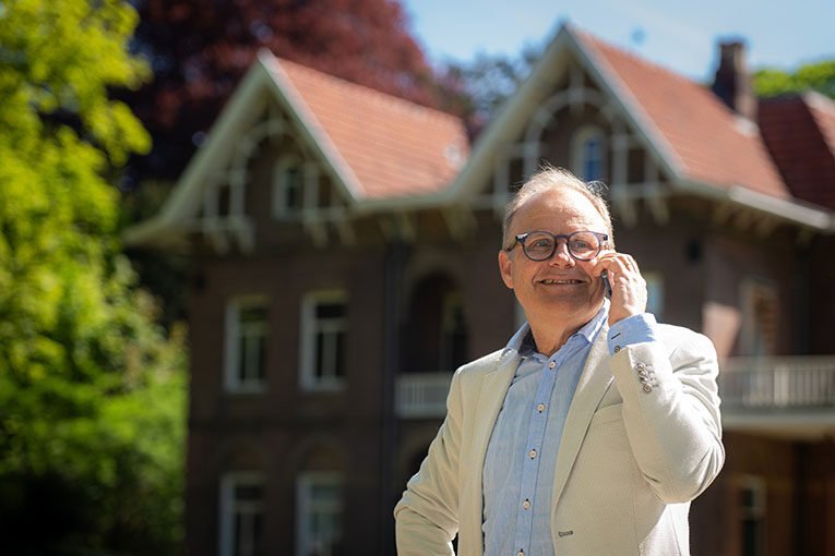 Makelaar staat lachend met een telefoon aan de oor